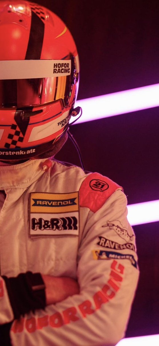 Torsten Kratz im Hofor-Racing-Rennanzug mit Helm, Neonlicht im Fahrerlager